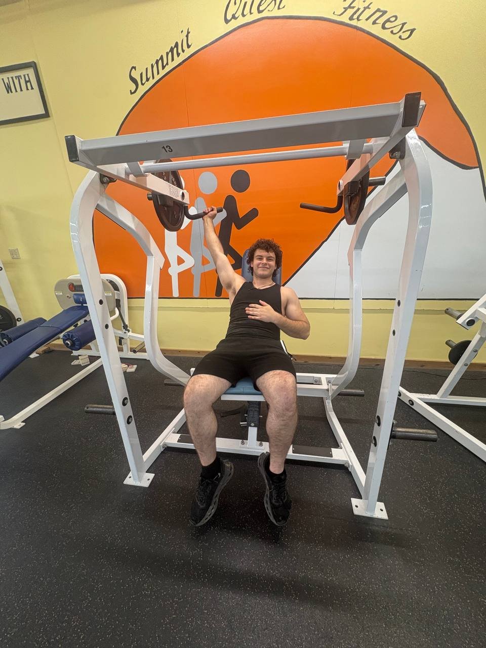 Member pressing overhead on the iso-lateral shoulder press in front of the Summit Quest mural